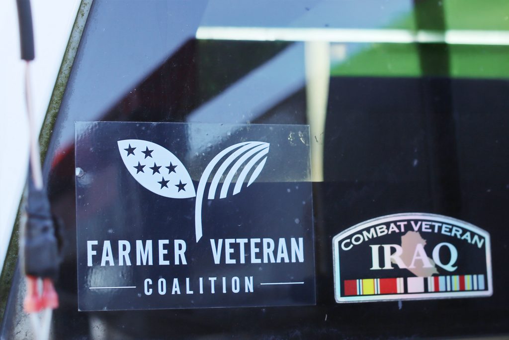Stickers on a window featuring the Farmer Veteran Coalition logo and a Combat Veteran Iraq emblem.