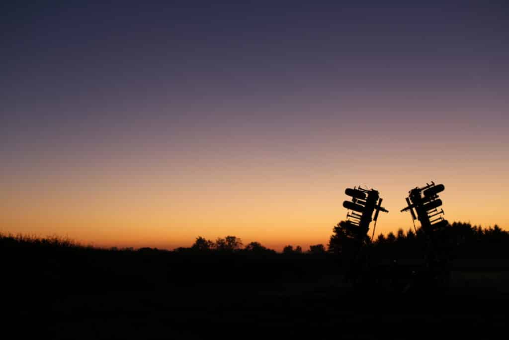Silhouette of farm equipment against an orange and purple sunset sky.